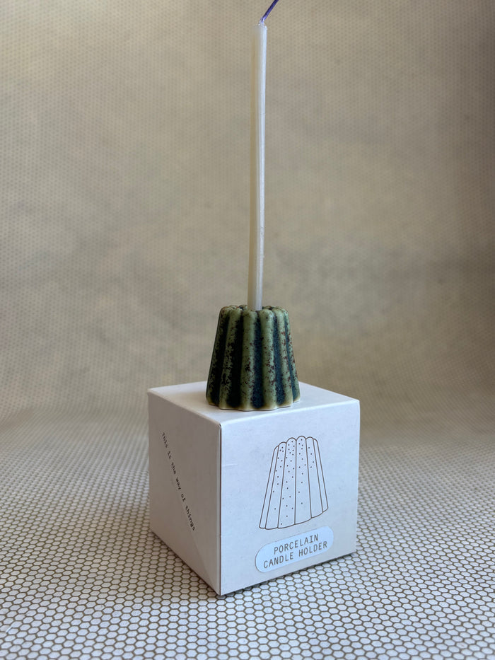 candle in small porcelain textured green candle holder on neutral background and small cardboard box.