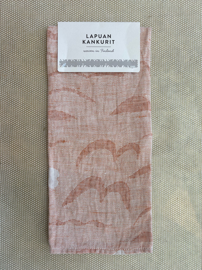 A folded woven fabric item with a white paper label at the top reading 'LAPUAN KANKURIT' and 'woven in Finland,' shown on a textured beige background.