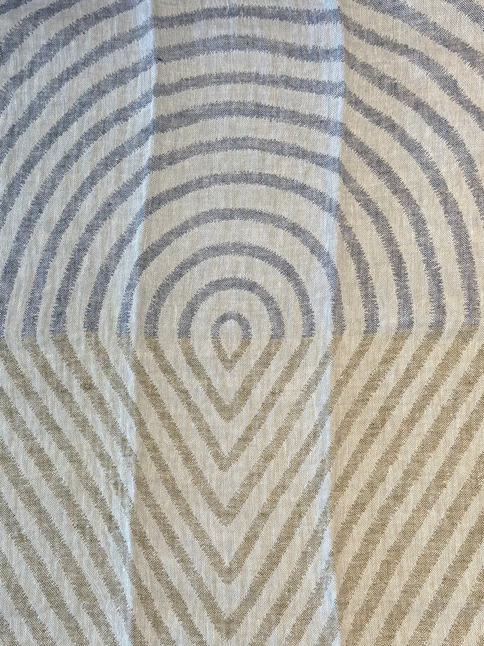 A close-up of a kitchen towel with a geometric pattern of concentric arches and chevrons in muted blue-gray and warm beige and green tones.