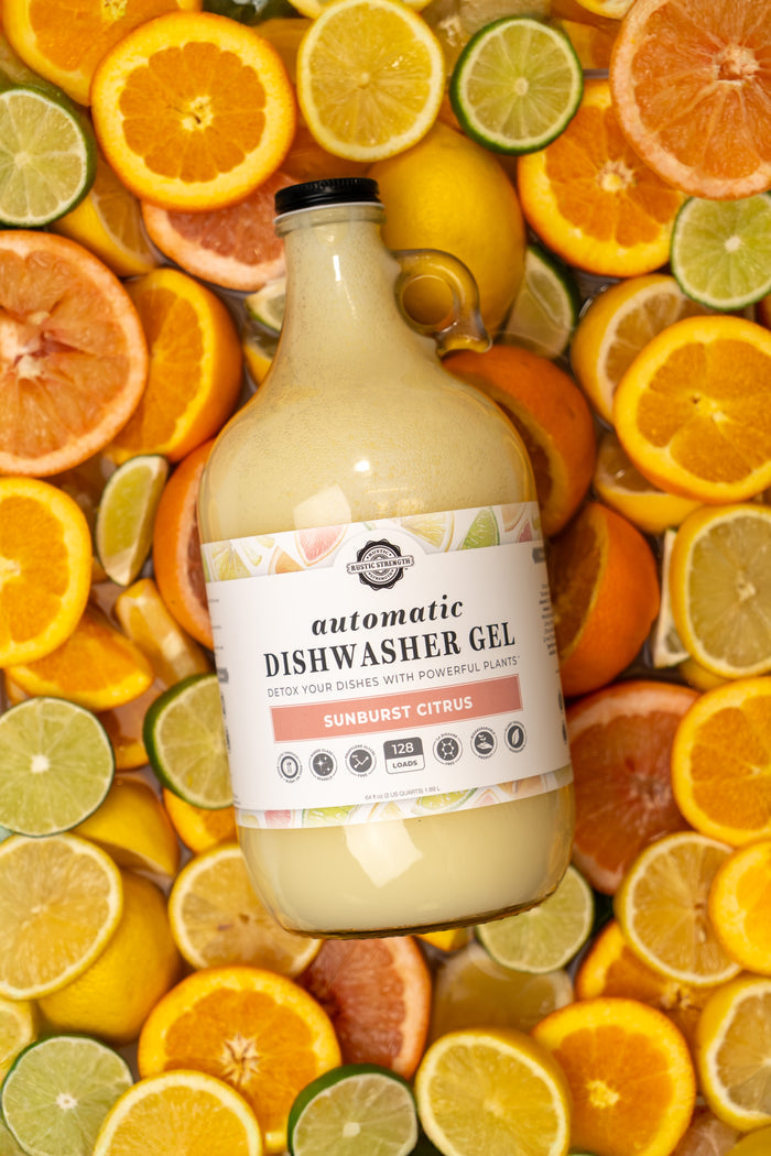 Rustic Strength, Automatic Dishwasher Gel, 64 oz Glass,Sunburst Citrus,Laying  on a bed of sliced citrus fruit