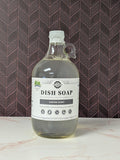 Rustic Strength, Dish Soap, Half Gallon, Glass Jug, Aromatherapy Blend, set on a light marbled surface with a patterned backdrop