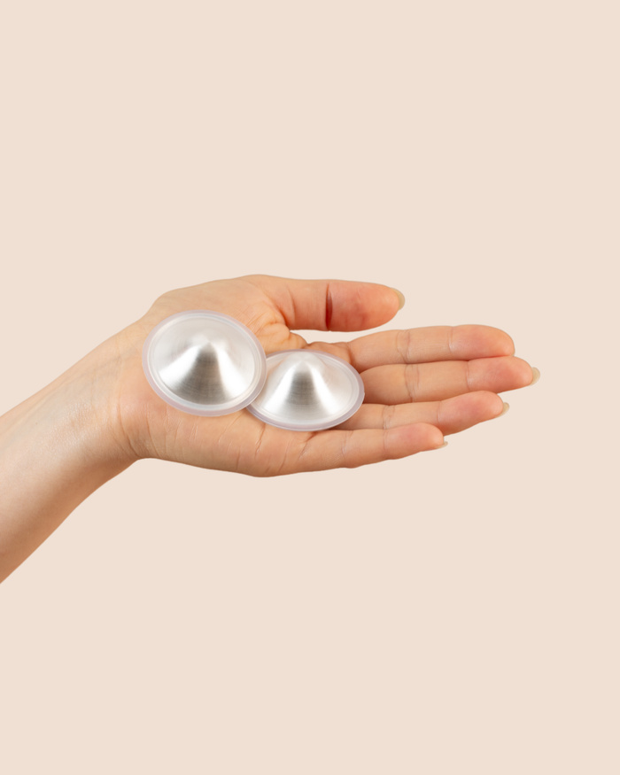 MammaBump silver nursing cups in pure 999 silver, shown in hand to soothe sore nipples between feeds