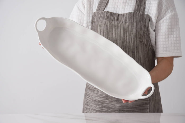 Person holding a white ceramic rolling pin with a plain background