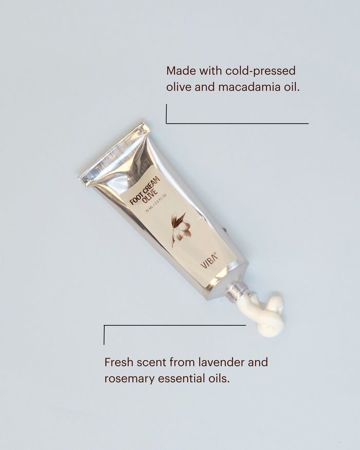 Beige foot cream tube with gold cap and sample dollop beside it on gray background.