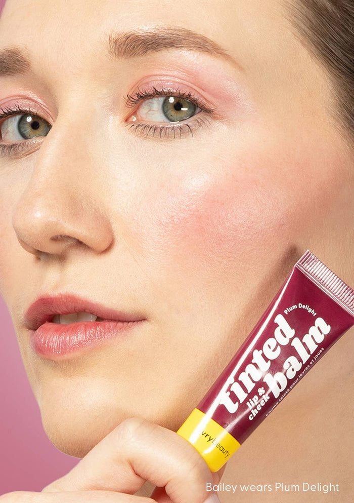 Woman holding a tube of tinted balm with a pink background