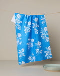 Blue towel with white floral pattern hanging on a line against a beige wall.