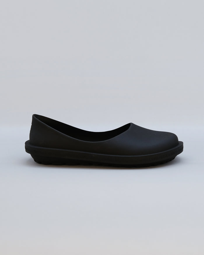 Black rubber slip-on shoe with curved design and textured sole, shown in side profile.