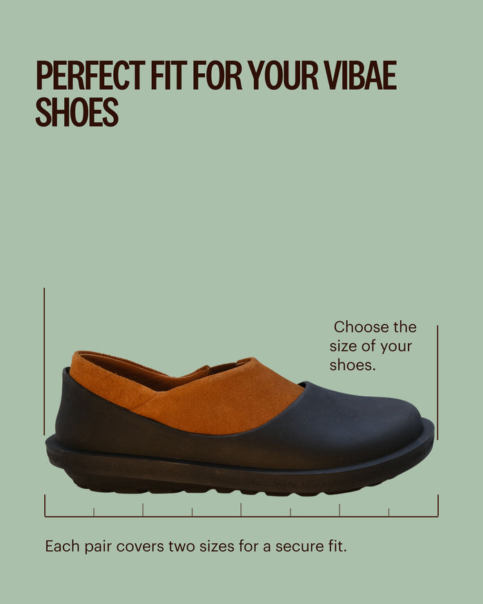Black and tan slip-on shoe with cushioned sole against green background.