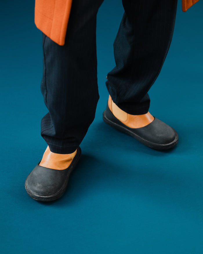 Black rubber clogs with tan leather trim worn with dark jeans and orange jacket.