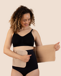 New mum wrapping the tan MammaBump Postpartum Belly Band around her waist for gentle postpartum recovery support after vaginal birth