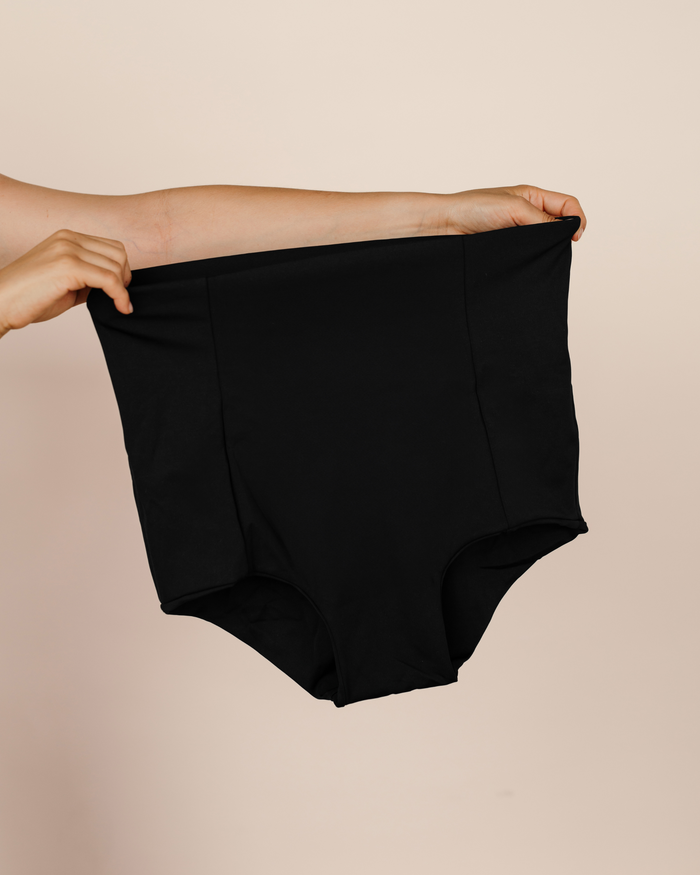 Hands holding up the black MammaBump Postpartum Soothing Brief, high-waisted and seamless for postpartum recovery