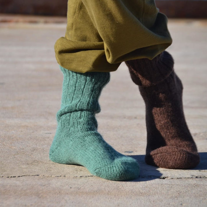 Person wearing olive-green pants and mismatched socks in turquoise and brown, standing on concrete ground.