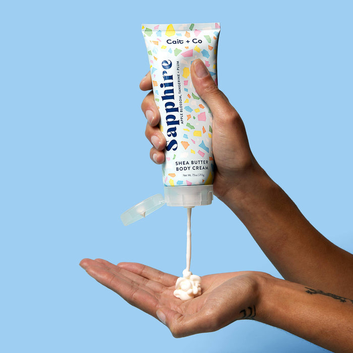 person squeezing sapphire body lotion onto their palm against a blue background