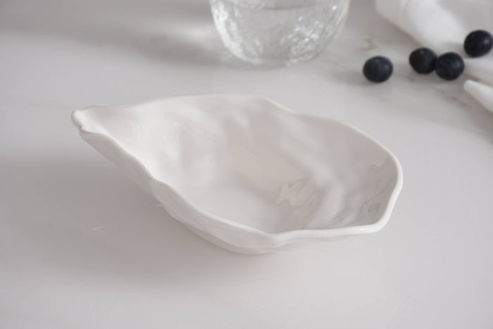 White ceramic leaf-shaped dish on a light surface with blueberries and a glass jar in the background.