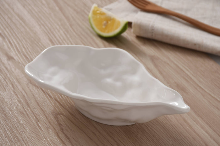White ceramic leaf-shaped bowl on a wooden surface with a lemon wedge and wooden spoon in the background.