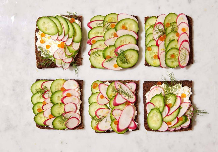 Six slices of bread with cucumber and radish slices on a light background