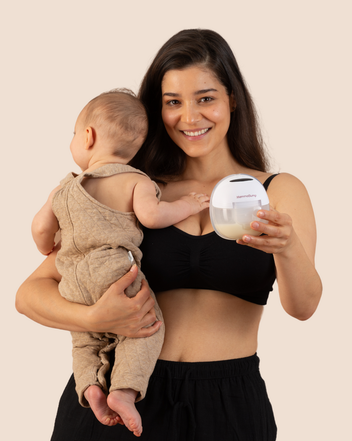 A woman is holding a baby and a wearable breast pump device